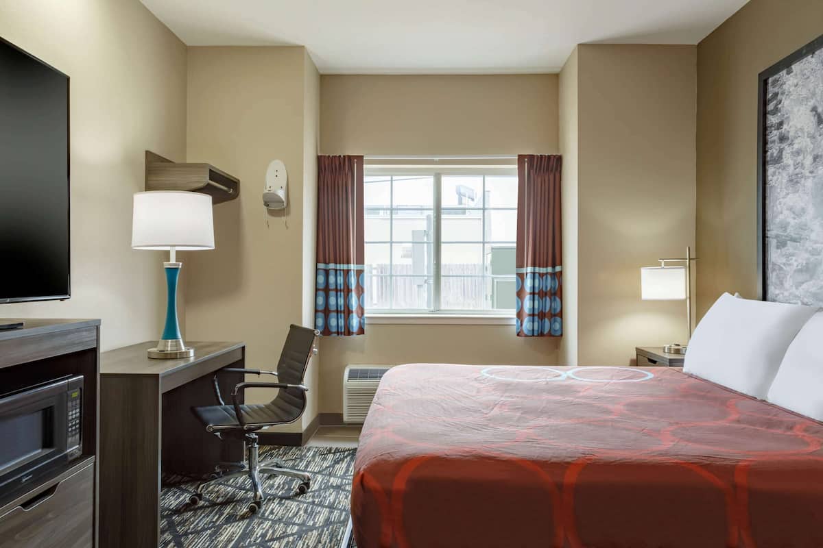 Une chambre d’hôtel équipée d’un lit, d’un bureau, d’une chaise, d’une télévision et d’une fenêtre avec des rideaux.