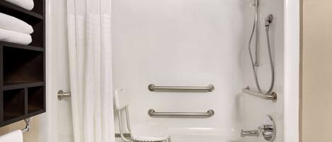 A bathroom with a bathtub, grab bars, a showerhead, and a white chair.