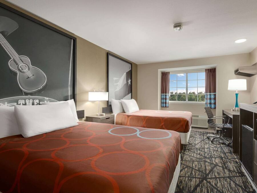 Habitación de hotel con dos camas, un escritorio, un televisor y una ventana con vistas.