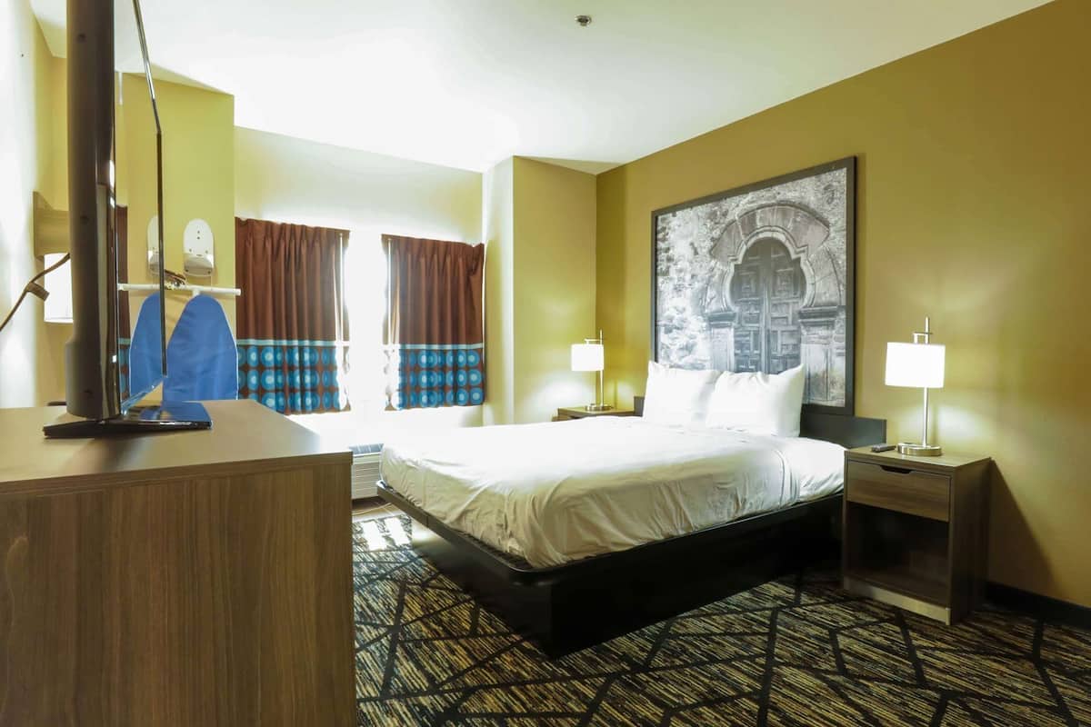 Une chambre d’hôtel avec un lit, une table de chevet, une lampe et une grande fenêtre avec des rideaux.