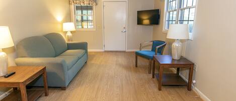Una sala de estar con sofá, dos sillones, una mesa de centro, televisor y puerta.