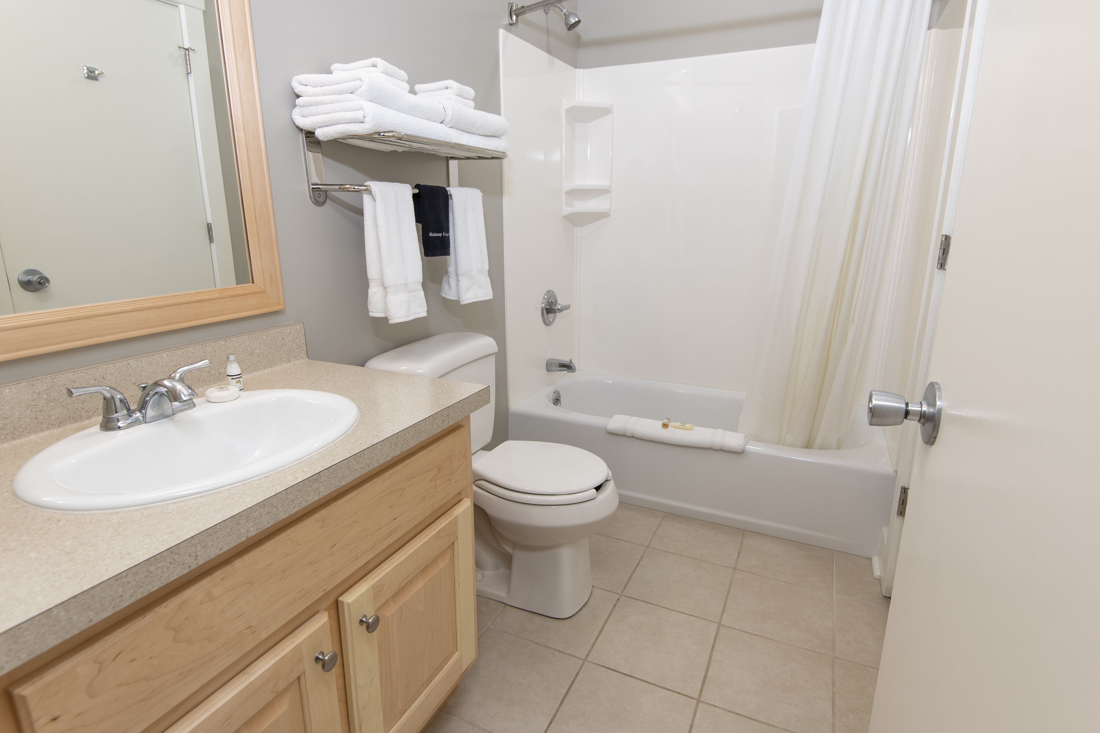 A bathroom with a sink, toilet, and bathtub. There are towels on a shelf and a towel hanging on the wall.
