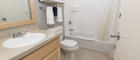 A bathroom with a sink, toilet, and bathtub. There are towels on a shelf and a towel hanging on the wall.