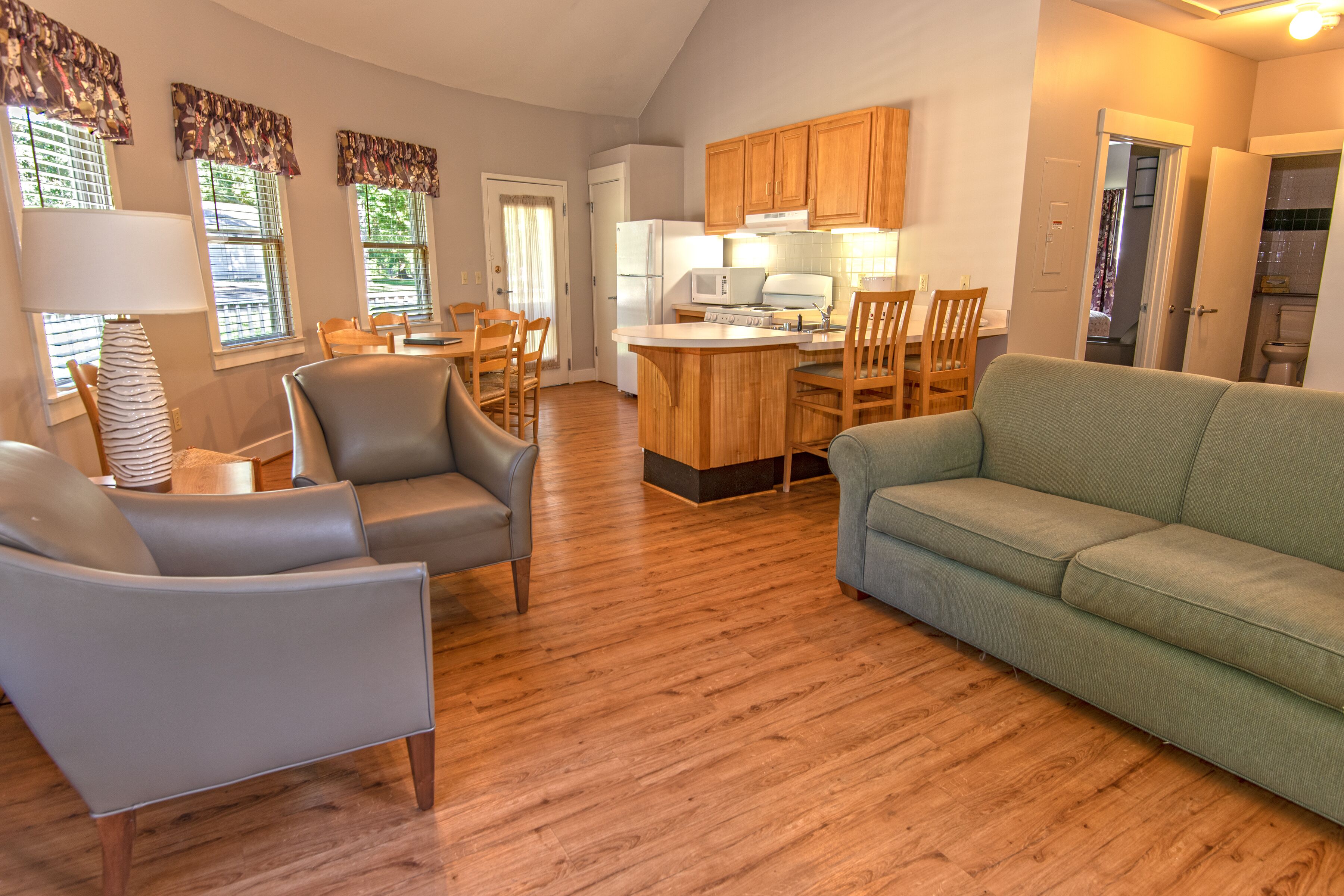 A spacious living area with a sofa, chairs, a dining table, and a kitchen with wooden cabinets and appliances.