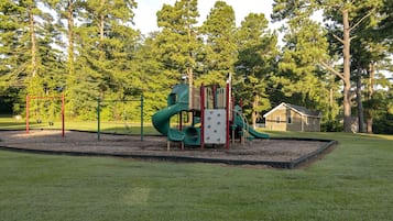 Children can play on the green slide, climbing structure, and red swing set in this well-maintained playground area.
