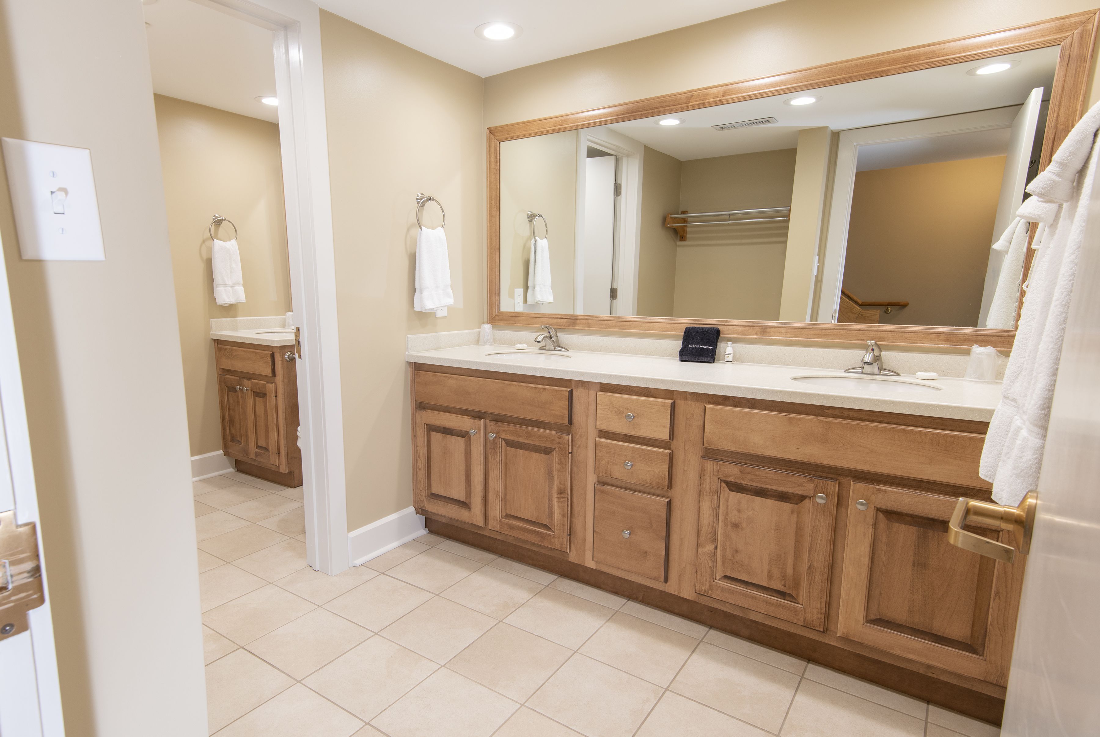 A bathroom with wooden cabinets, a large mirror, and a white countertop.