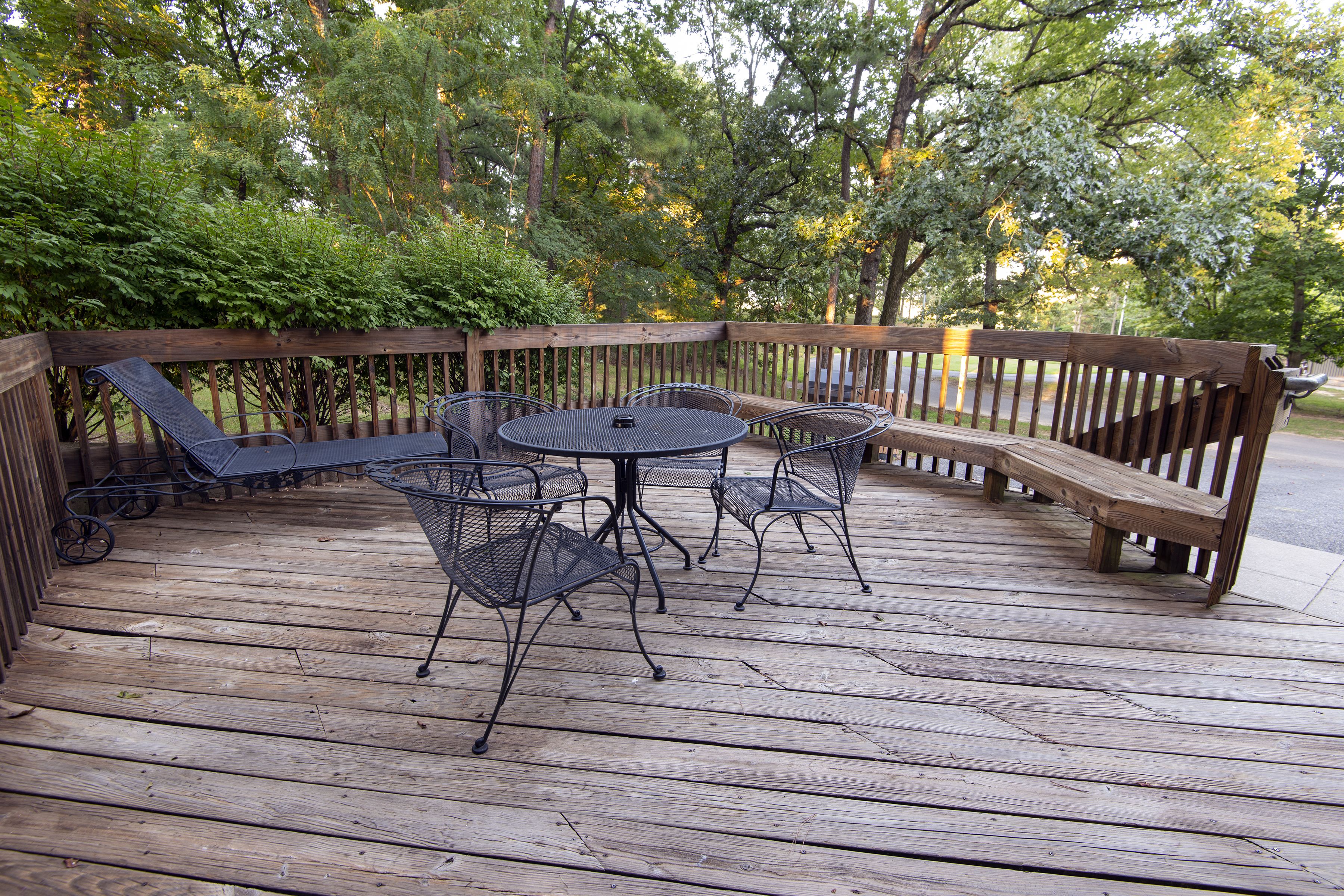 Une terrasse en bois avec une table et des chaises, entourée d’une clôture en bois et d’arbres.