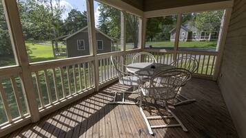 A covered outdoor deck with a table and chairs, overlooking a grassy yard and houses.