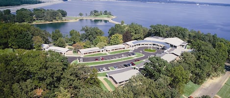 An aerial view of a hotel with a parking lot, a lake, and surrounding greenery.