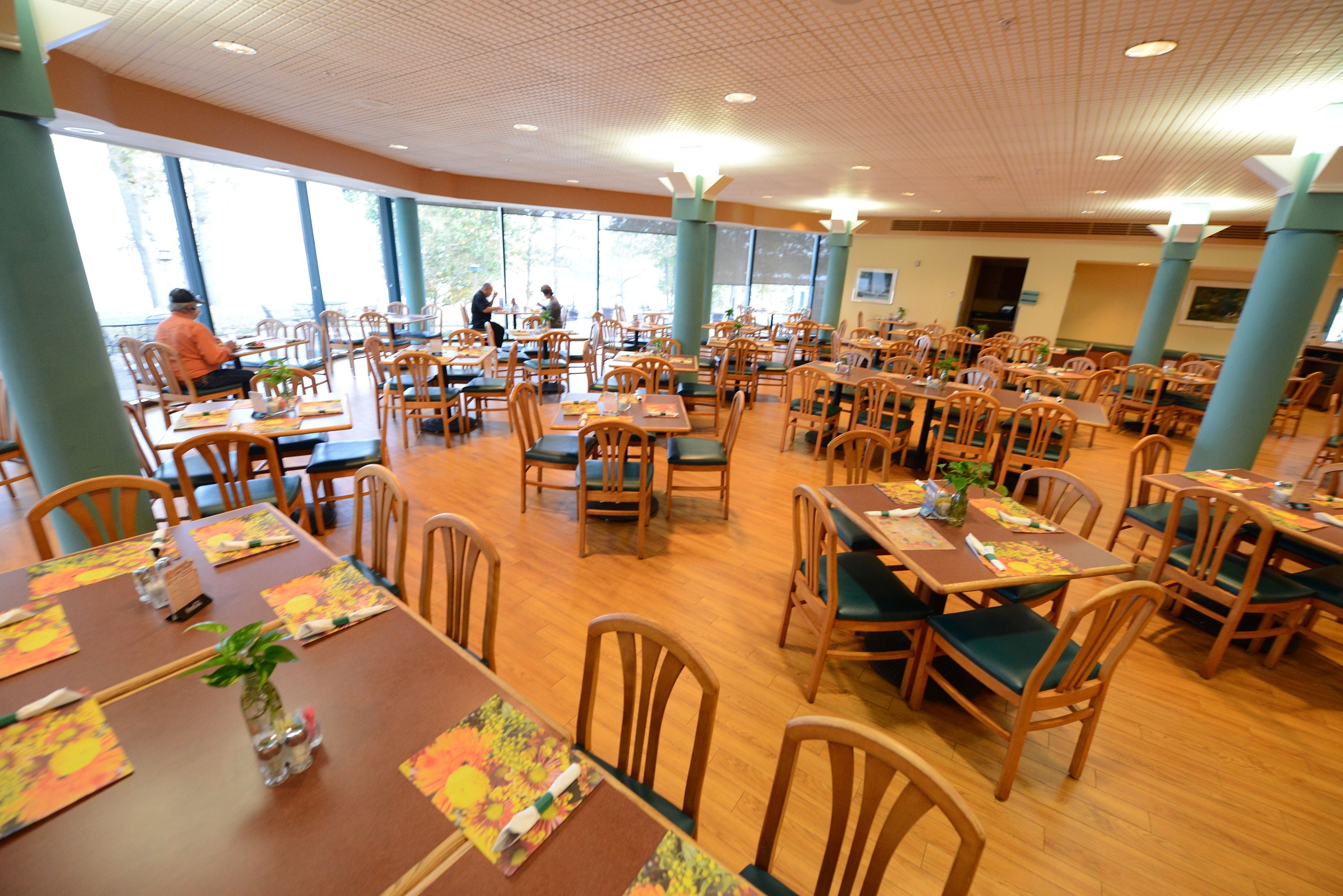 A spacious dining area with multiple tables and chairs, large windows, and a high ceiling.