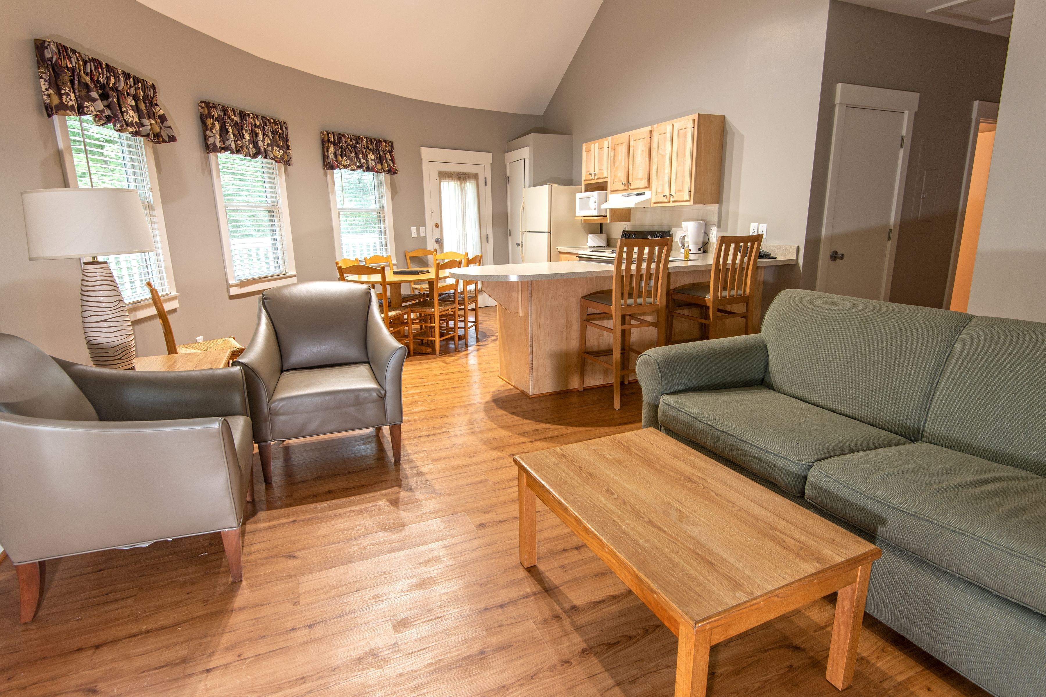 A modern living room with a sofa, chairs, a coffee table, and a kitchen area with wooden cabinets and a dining table.