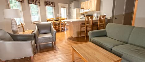 A modern living room with a sofa, chairs, a coffee table, and a kitchen area with wooden cabinets and a dining table.