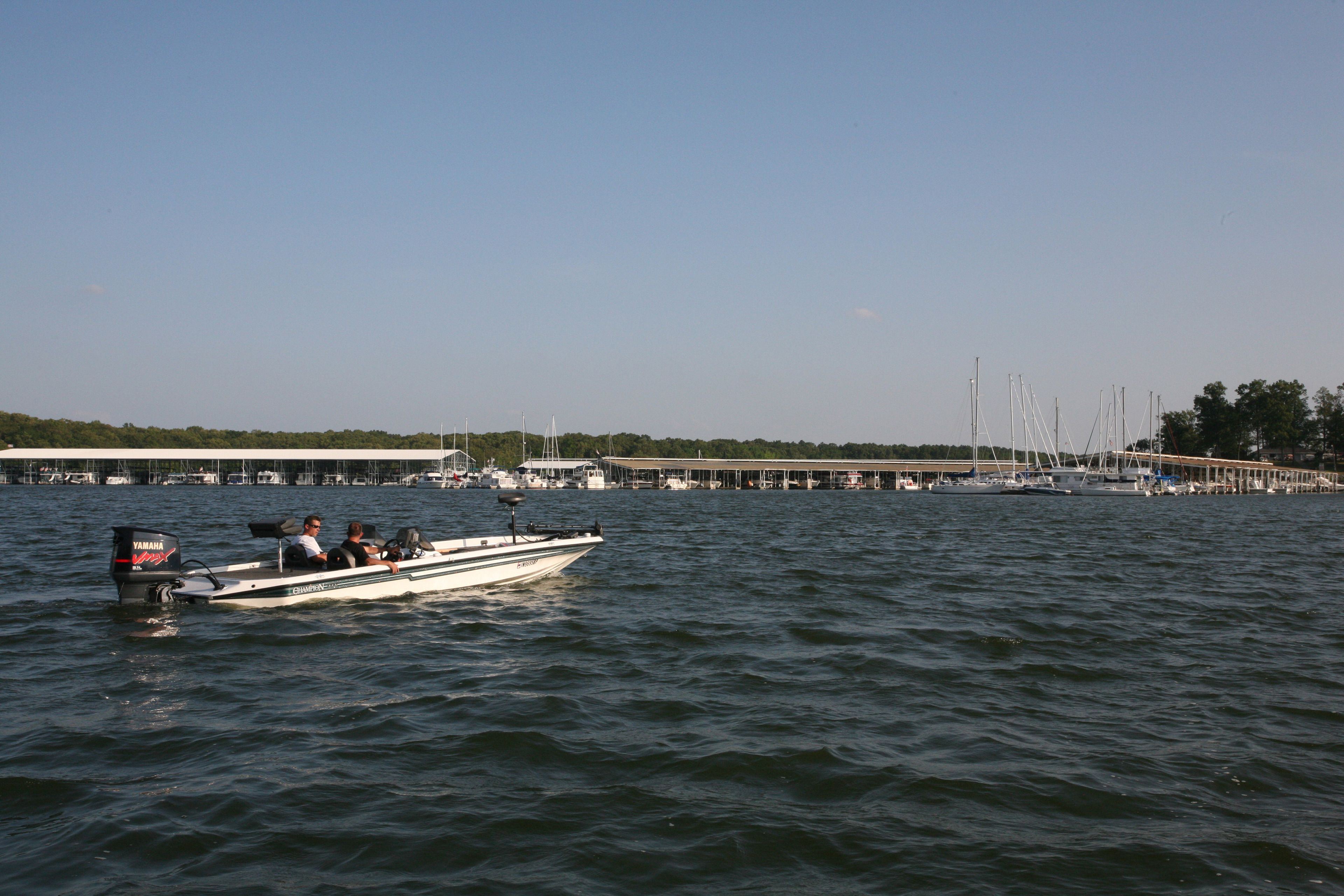 Un bote sobre el agua, con un embarcadero y un puerto deportivo al fondo.