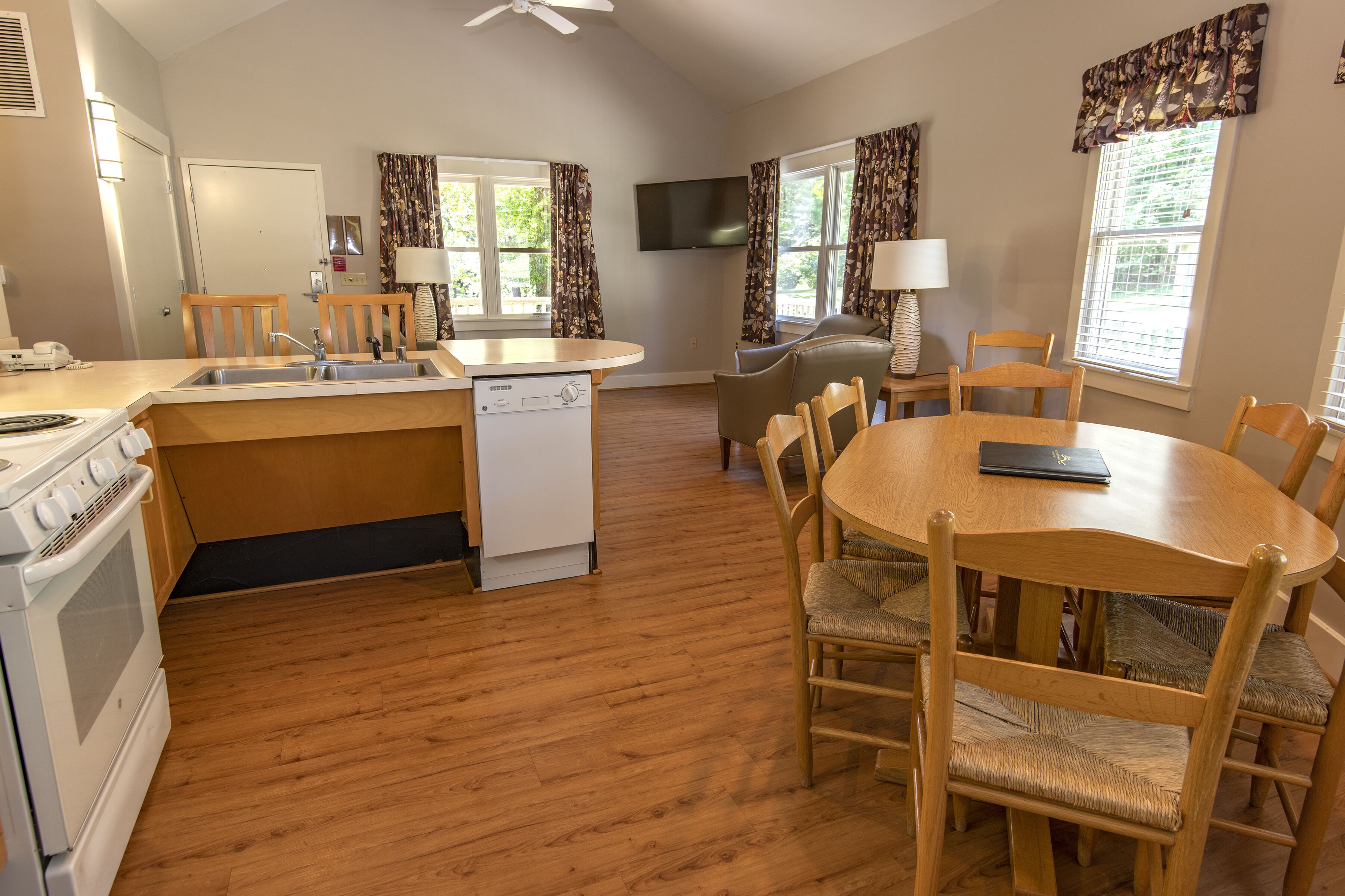 A kitchen with wooden cabinets, a dishwasher, and a stove. There is a dining area with a round table and chairs.