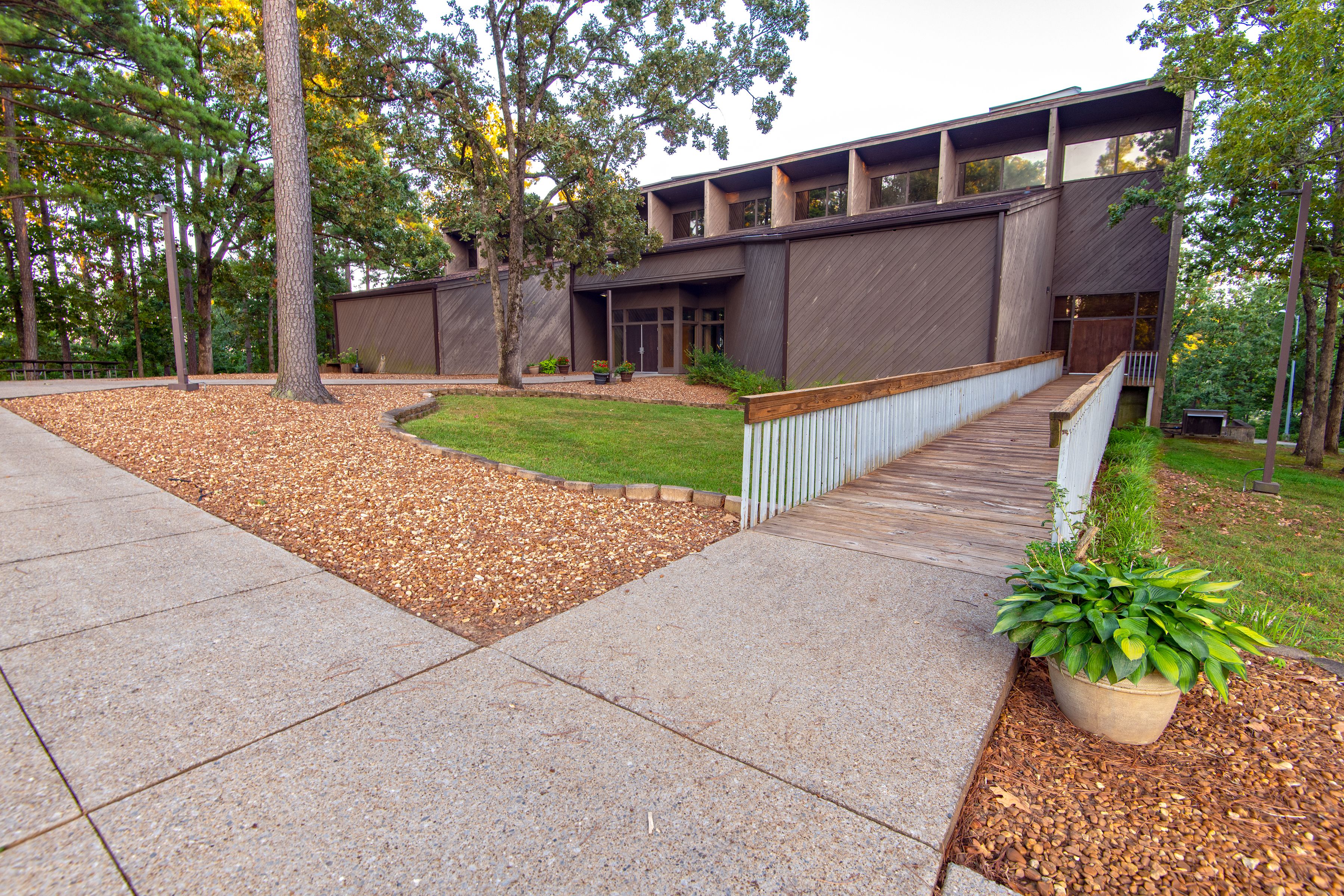 A modern building with a flat roof, large windows, and a wooden deck leading to the entrance.