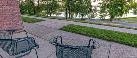 A metal outdoor seating area with a metal chair and a metal table, located near a brick wall and a paved path.