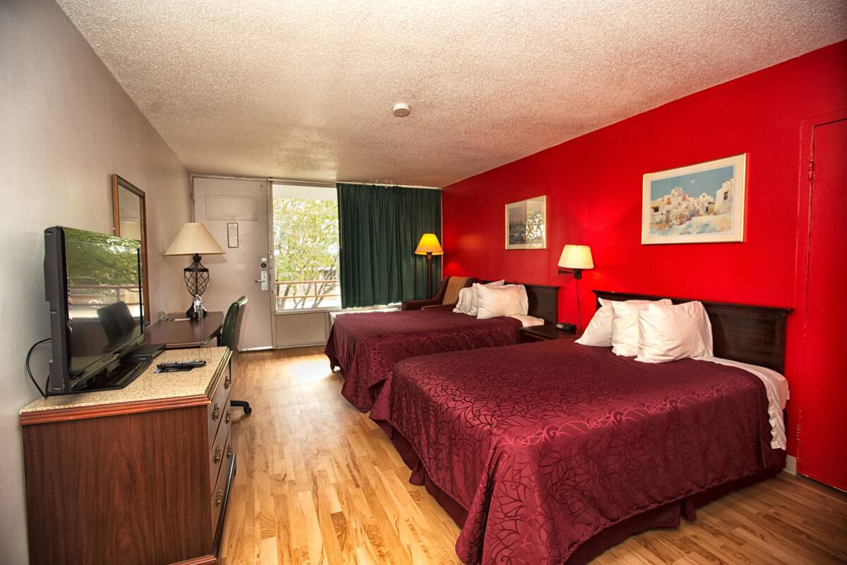 Una habitación de hotel con dos camas, un escritorio con televisor y una ventana con cortinas.