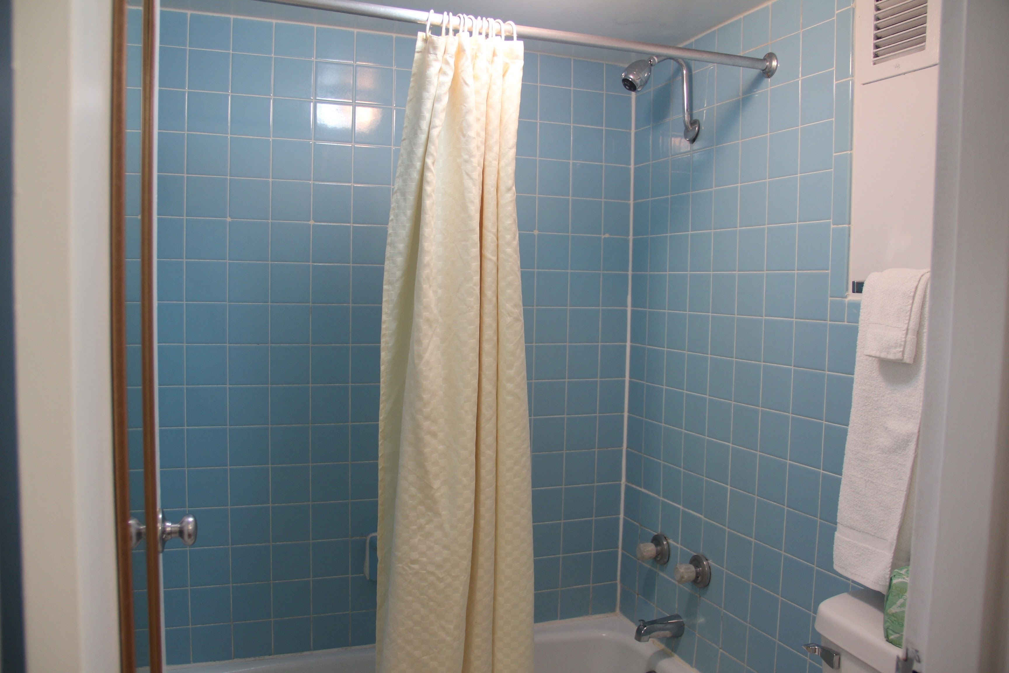 Un baño con azulejos azules, una ducha con cortina color beige, una bañera blanca y una toalla blanca colgada en la pared.