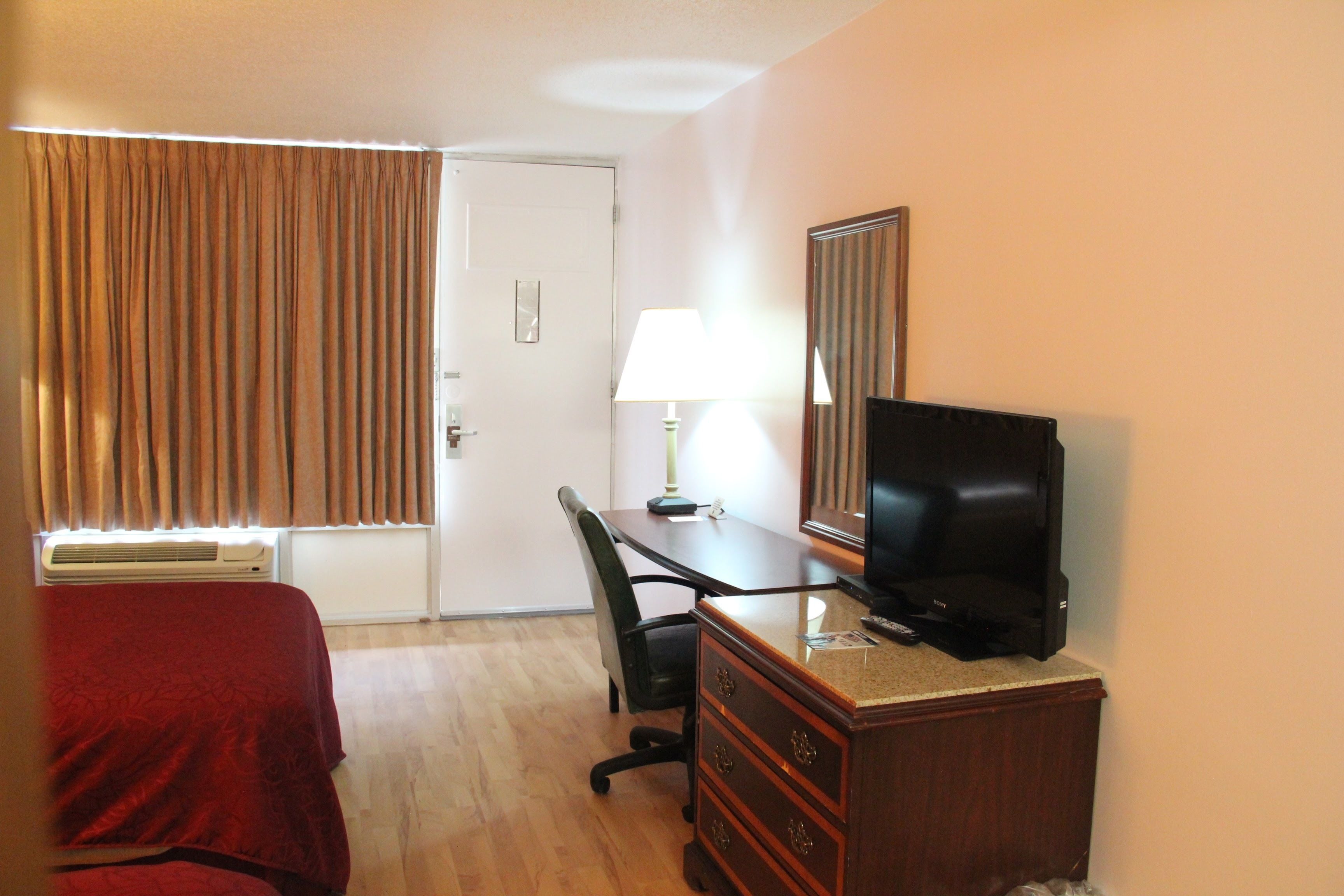 Une chambre d’hôtel comprenant un lit, un bureau avec une télévision, une chaise, une commode et une fenêtre avec des rideaux.