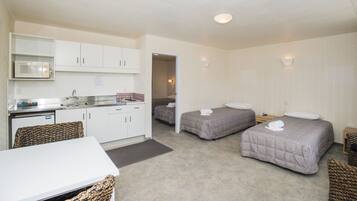 Habitación de hotel compacta con dos camas individuales, kitchenette, zona de comedor y baño.
