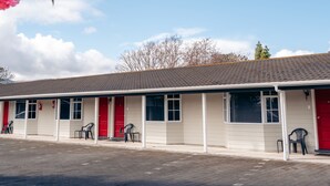 Un motel con una hilera de habitaciones, cada una con una puerta roja, y un estacionamiento al frente.