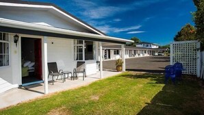 Un motel con un área de estar techada al aire libre, césped y una valla blanca.