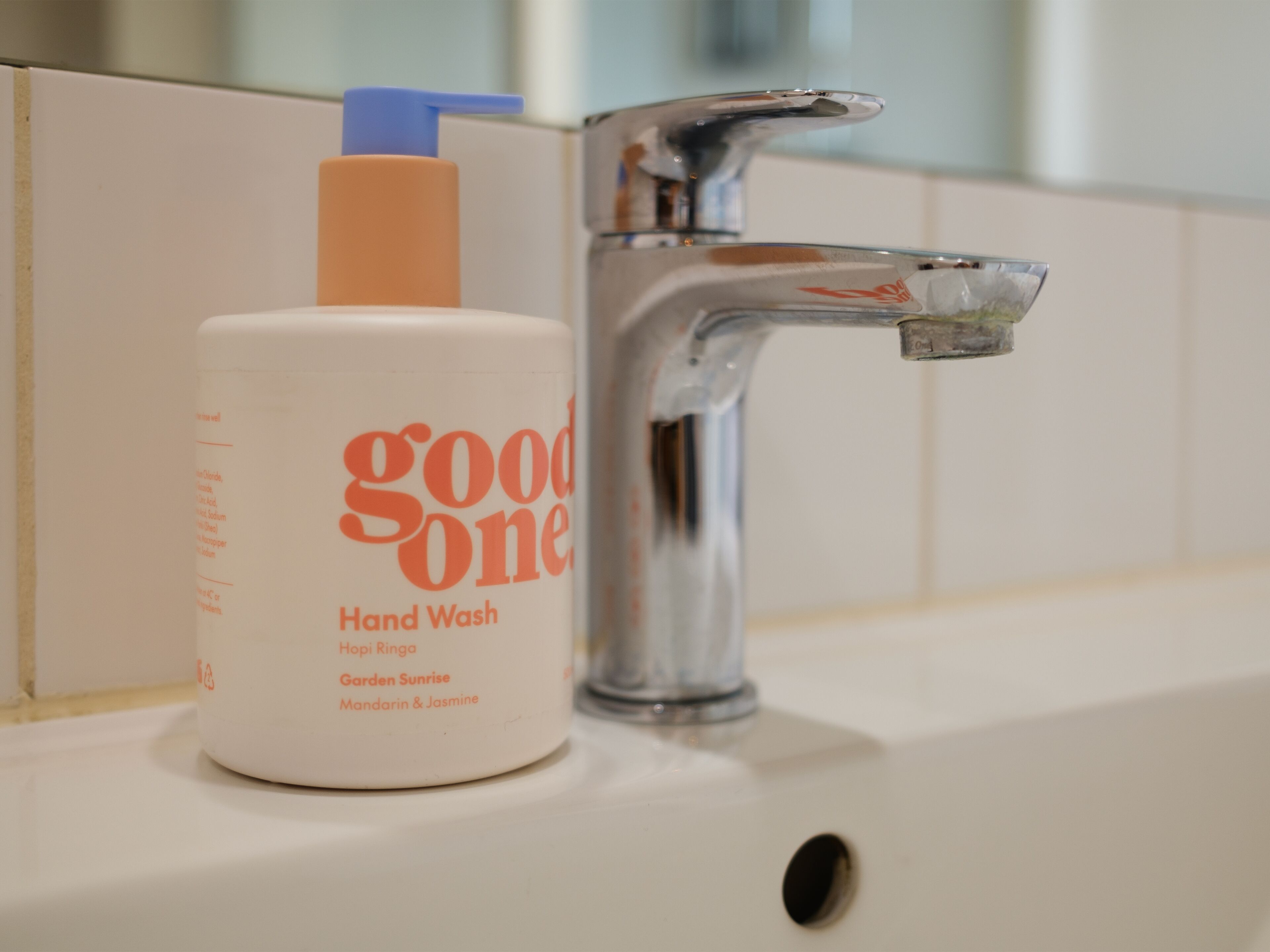 A bathroom sink with a bottle of hand wash soap labeled "good one" and a chrome faucet.