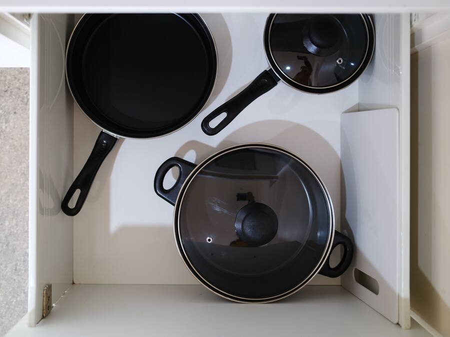 Un armario de cocina con tres ollas y sartenes negras.