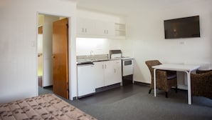 Habitación compacta con kitchenette, cama, zona de comedor con mesa y sillas, y televisor montado en la pared.