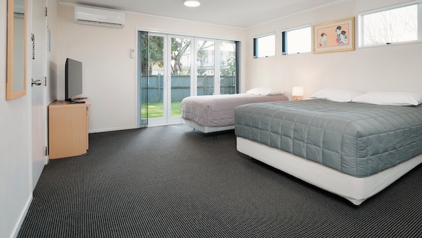 Una habitación de hotel con una cama grande, un televisor sobre un soporte, una puerta corrediza de vidrio al exterior y un mueble pequeño.