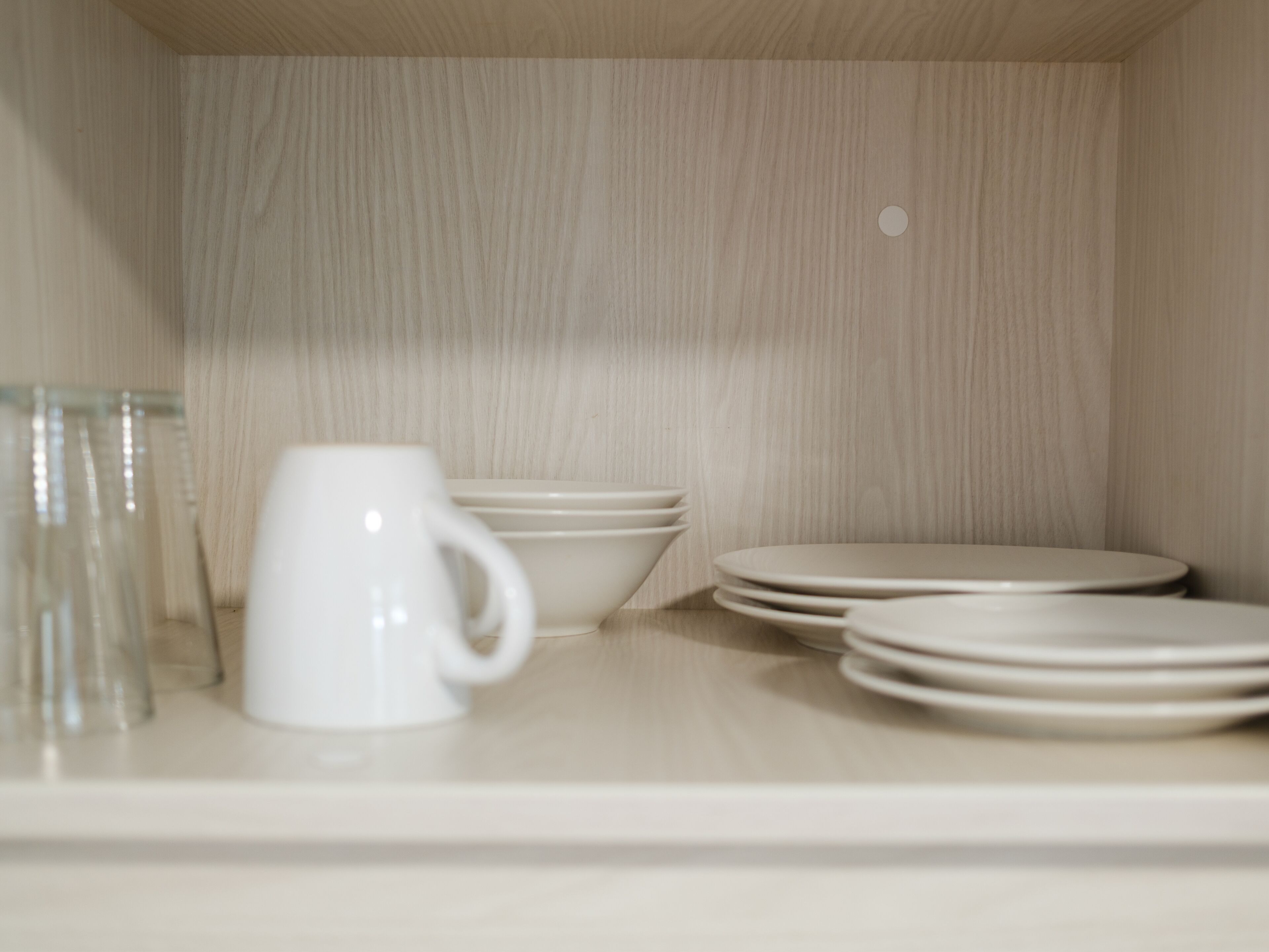 A storage area with shelves holding white mugs, bowls, and plates.