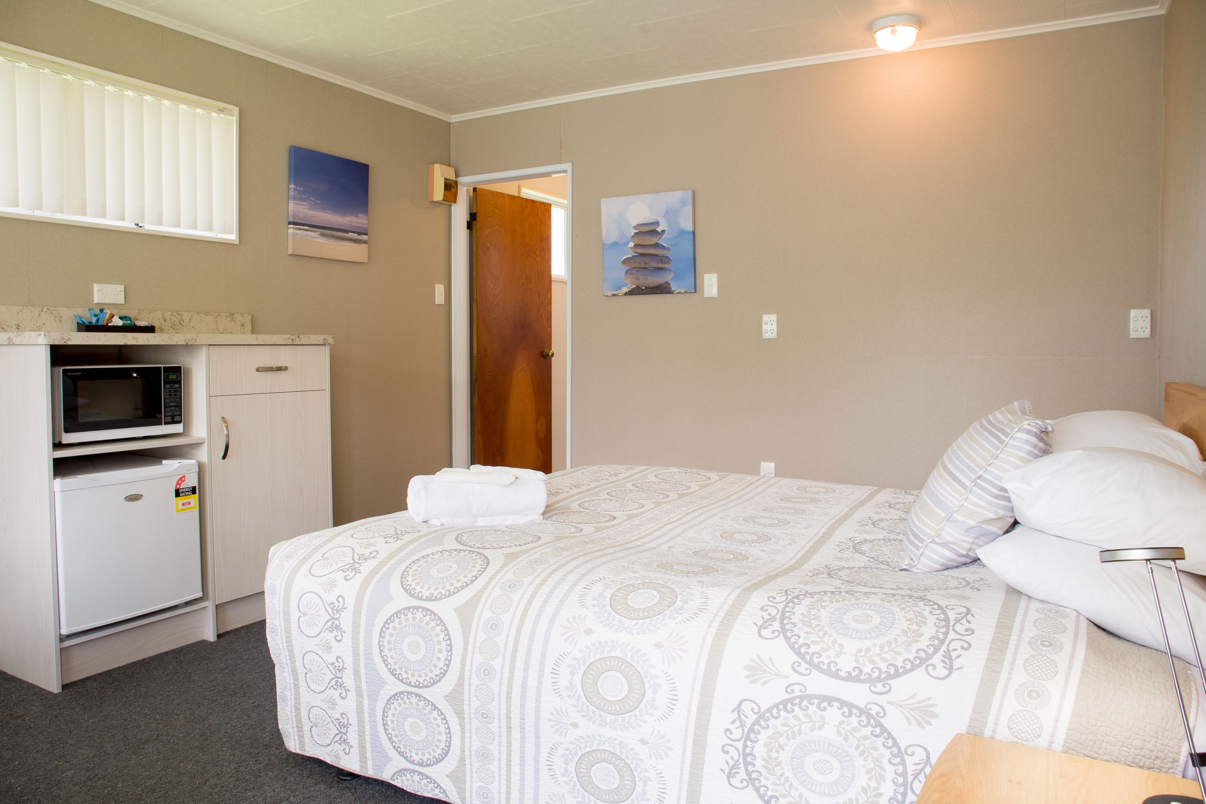 Un dormitorio con cama, almohadas, una lámpara de noche, un microondas y un refrigerador.