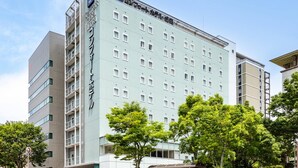 Un hôtel moderne, composé de plusieurs étages, doté d’une entrée imposante et d’un espace extérieur aménagé avec des sièges, protégé par un auvent.