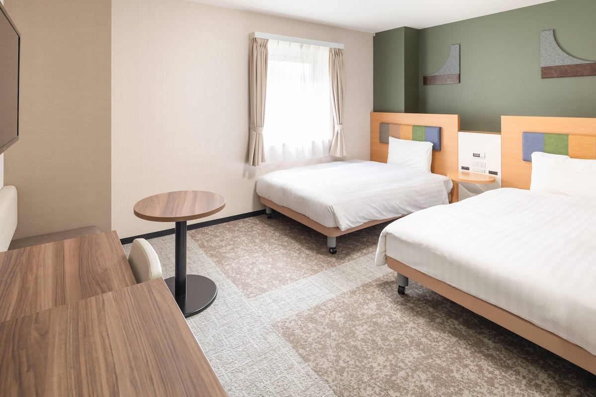 Een hotelkamer met twee bedden, een klein rond tafeltje en een televisie.