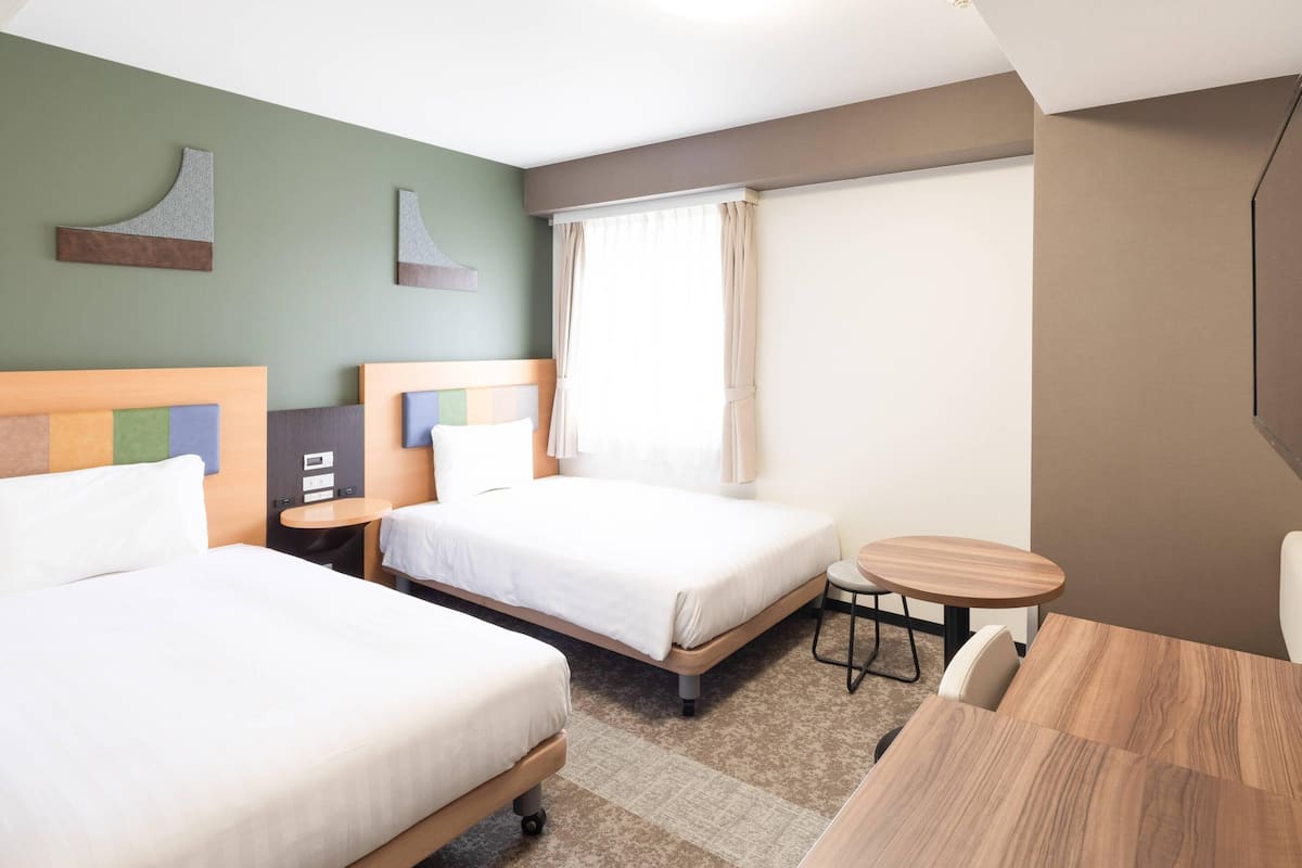 Een hotelkamer met twee bedden, een klein rond tafeltje, een stoel en een raam met gordijnen.