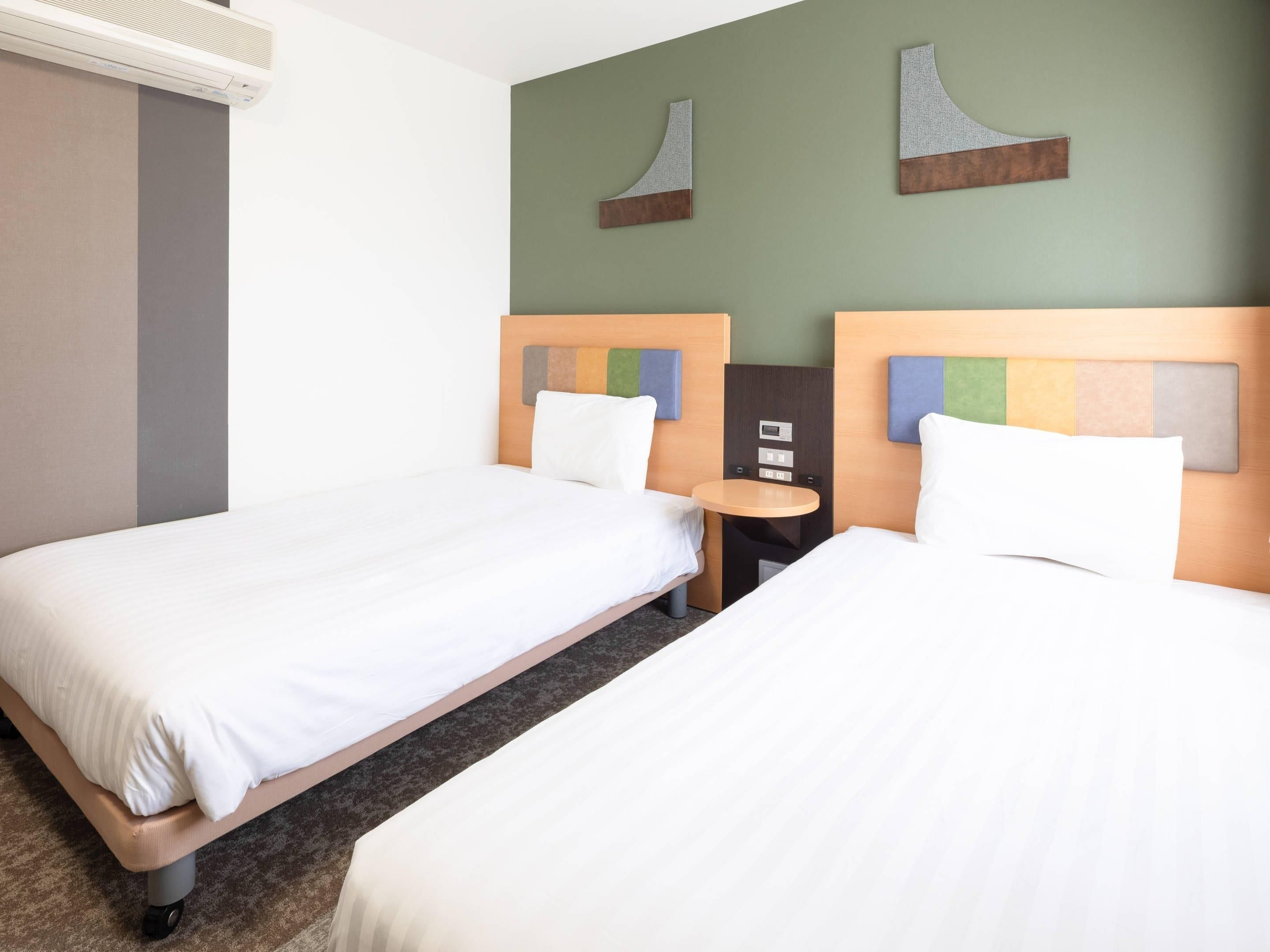 A hotel room with two single beds, a small round table, and a wall-mounted control panel.