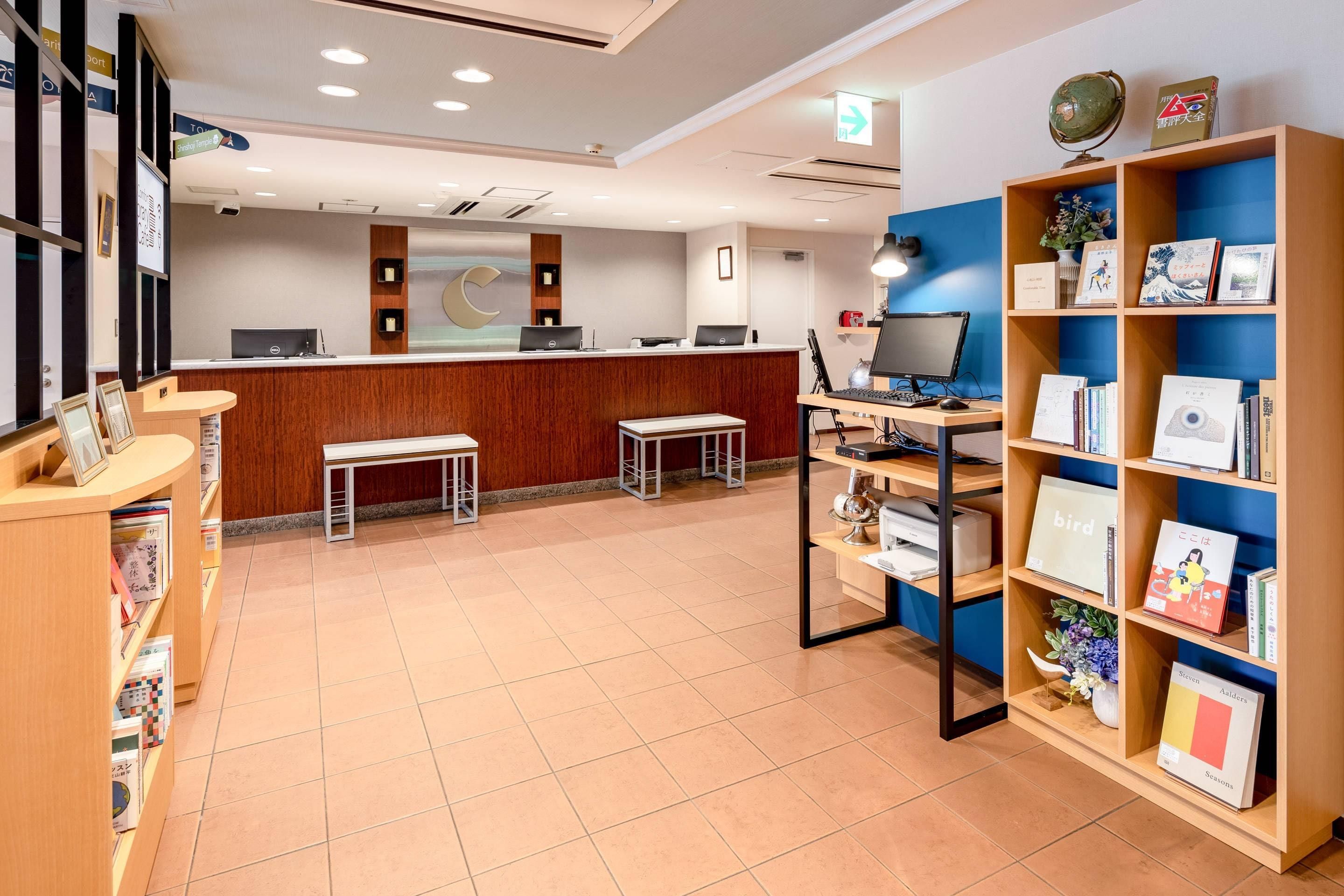Un área de recepción con un escritorio de madera, computadoras, un banco y una estantería con libros y objetos decorativos.