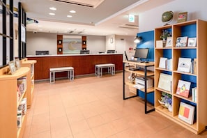 A reception area with a wooden desk, computers, a bench, and a bookshelf with books and decorative items.