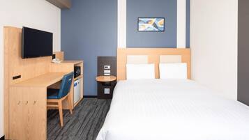 A hotel room with a bed, a desk with a chair, a television, a small table, and a wall-mounted artwork.
