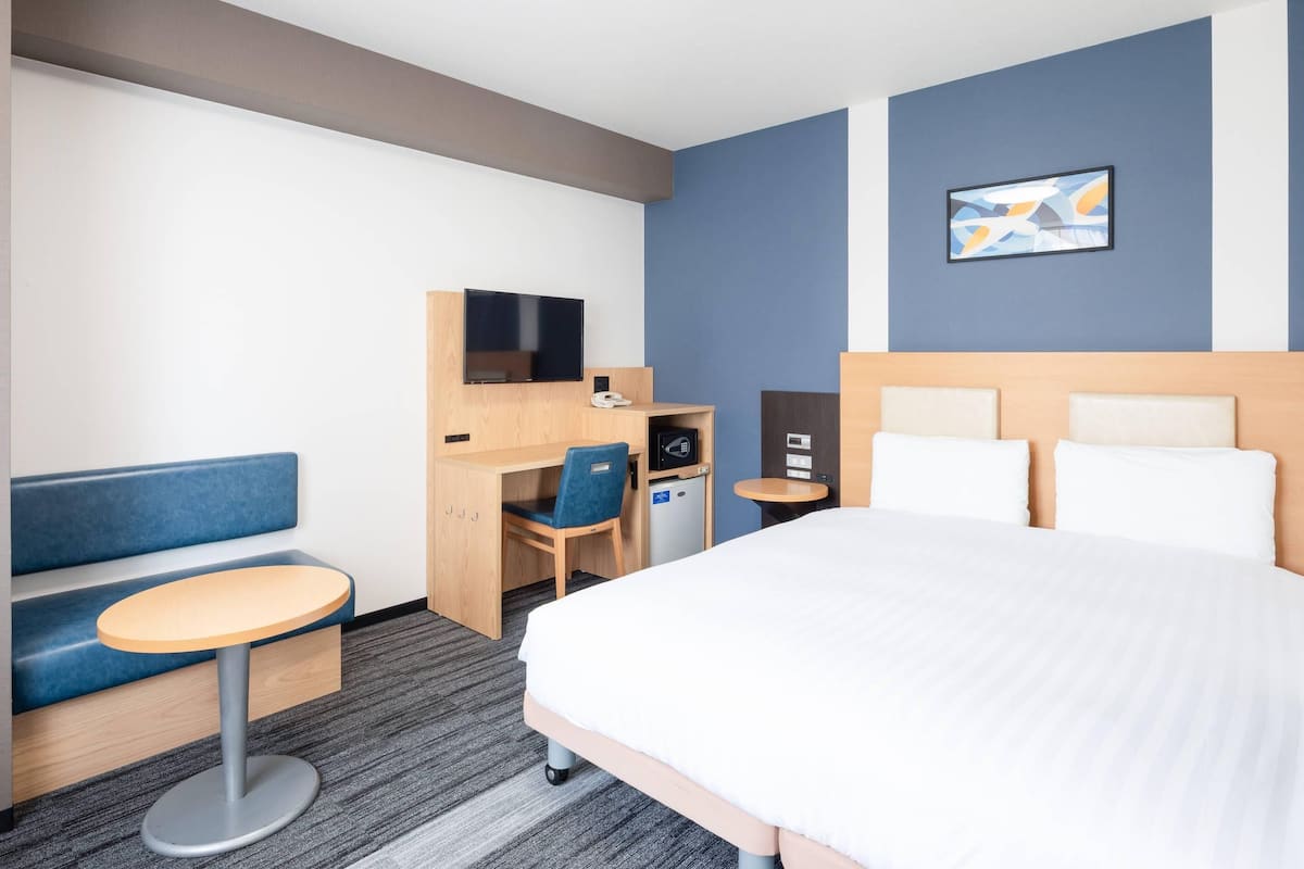 Hotelkamer met een bed, een bureau met stoel, een kleine tafel, een televisie en een aan de muur bevestigd telefoon.