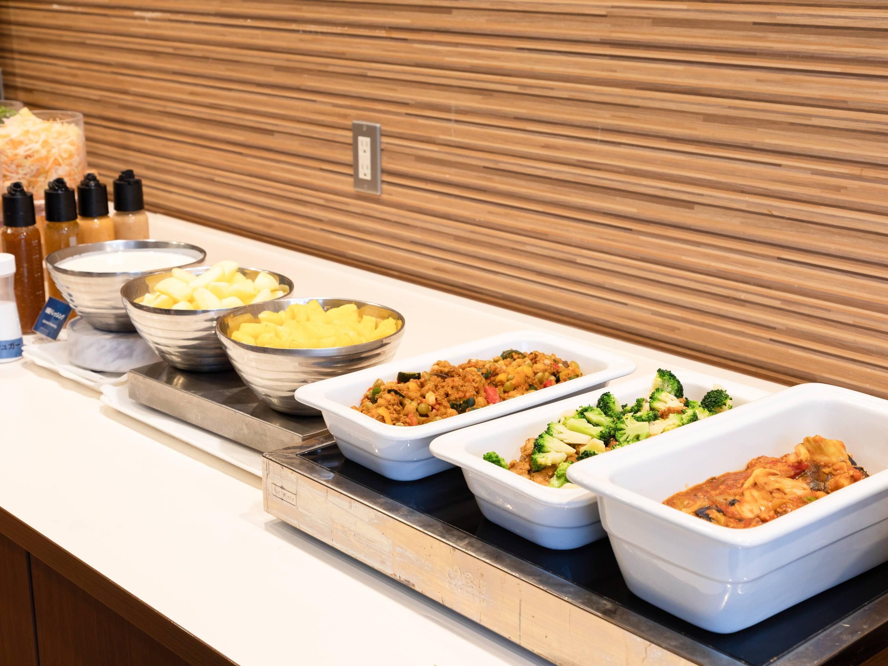 A buffet line with various dishes including potatoes, a vegetable mix, and pasta.