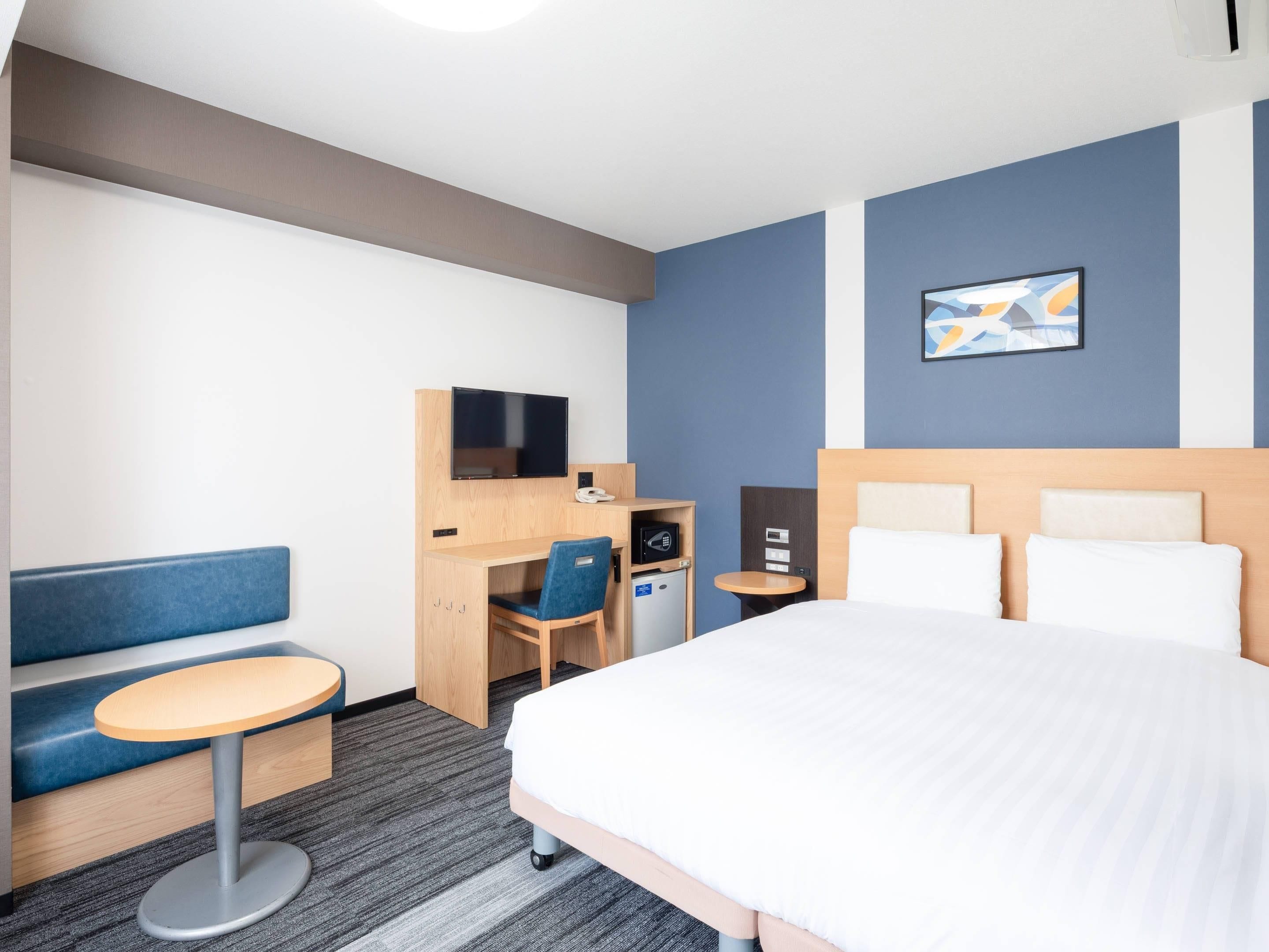 Habitación de hotel con cama, escritorio con silla, mesita pequeña, televisor y teléfono en la pared.