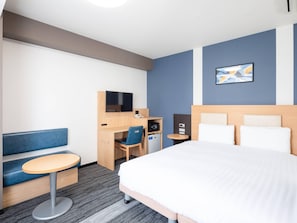 Habitación de hotel con cama, escritorio con silla, mesita pequeña, televisor y teléfono en la pared.