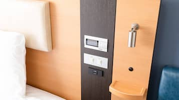 Ein Hotelzimmer mit einem Bett, einer Bedienkonsole mit Tasten für Zimmer und Fuß, einem kleinen Waschbecken und einer Tür mit Griff.