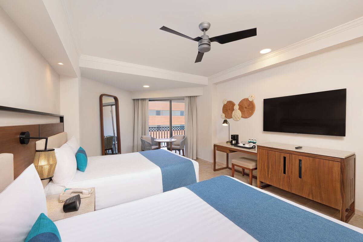 A hotel room with two beds, a desk, a chair, a television, and a balcony view.
