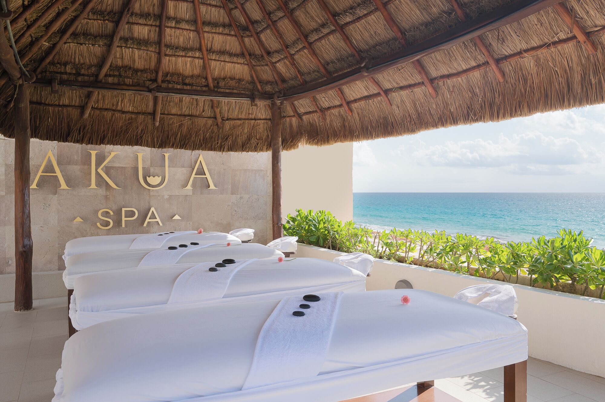 A spa area with a thatched roof, a sign reading 'AKUA SPA', and a view of the ocean.
