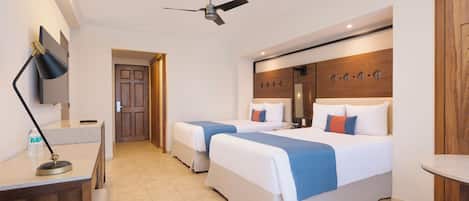 Une chambre d’hôtel avec deux lits, un bureau avec une lampe, un ventilateur de plafond et une tête de lit en bois agrémentée d’éléments décoratifs.