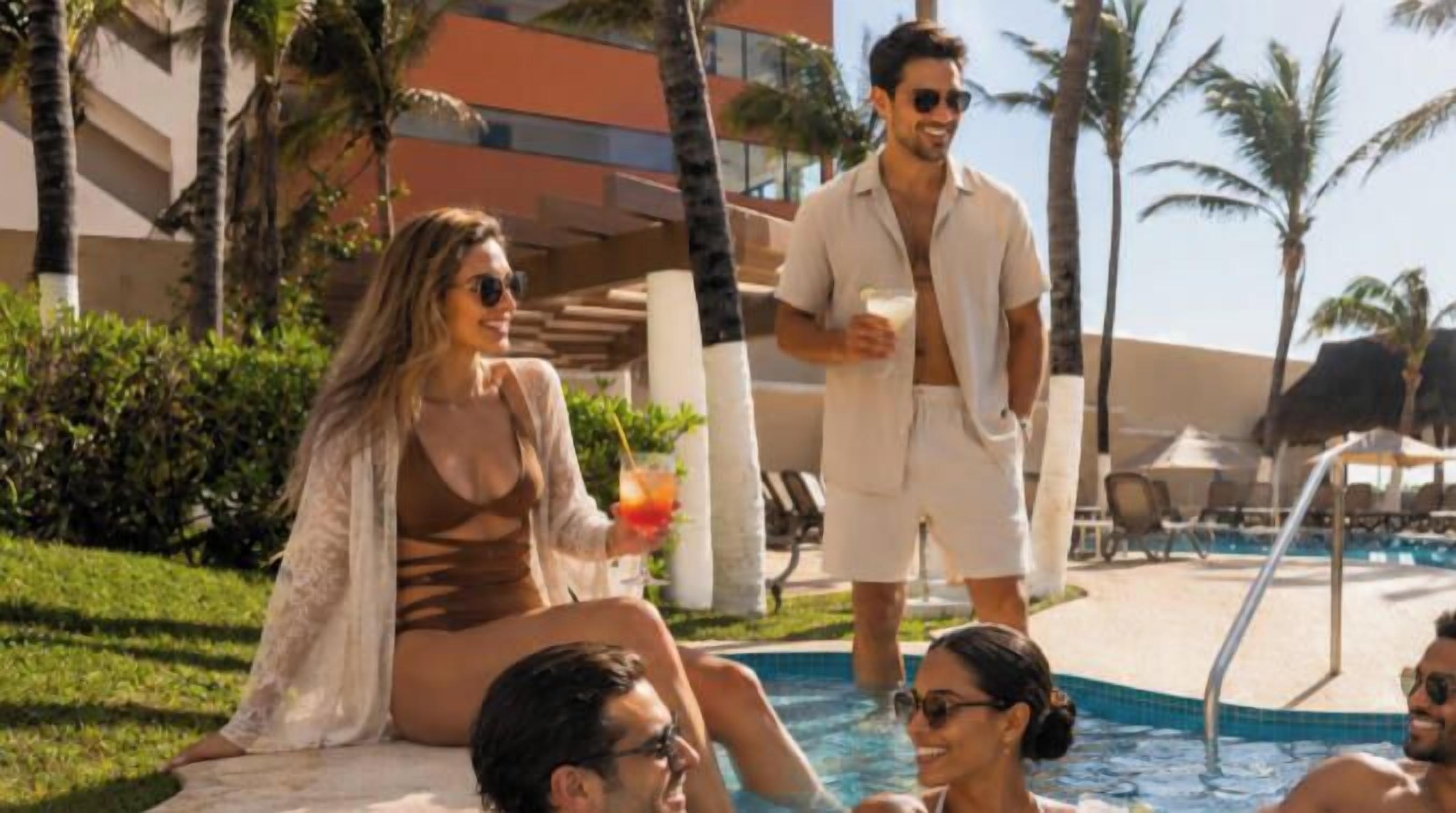 A poolside area with people relaxing, a clear sky, and palm trees.