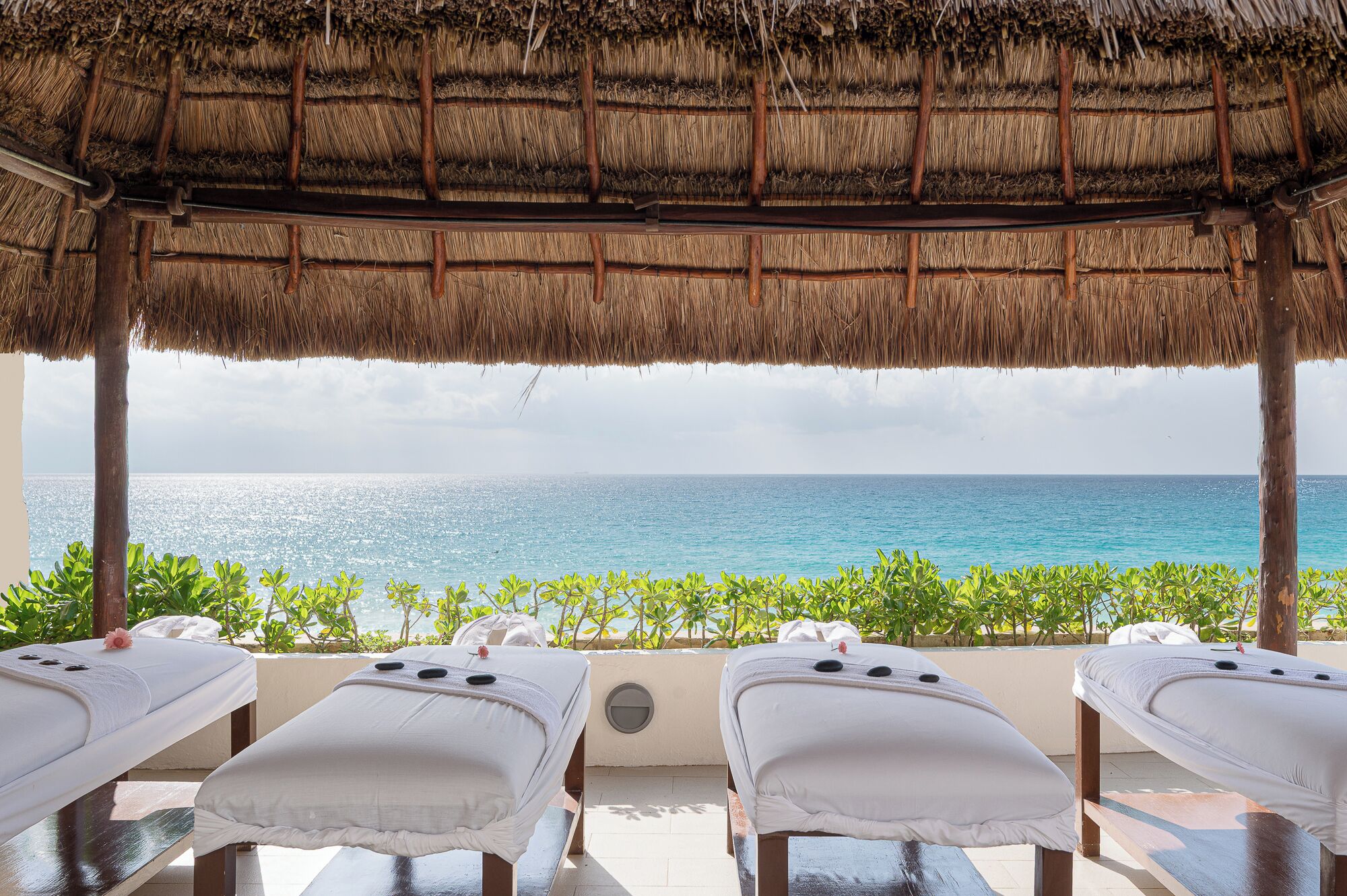 A beachside spa with thatched roof, three massage tables, and a view of the ocean.