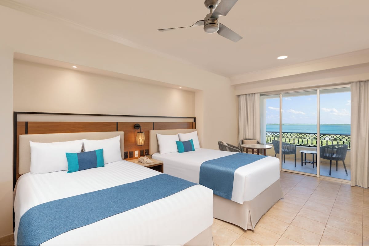 A hotel room with two beds, a balcony with a view, and a ceiling fan.